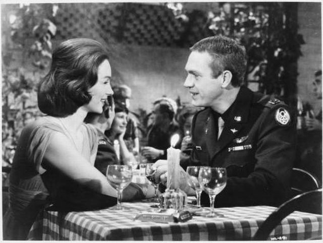 Shirley Anne Field (as Daphne) and Steve McQueen (as Buzz Rickson) talk over a candlelit table.